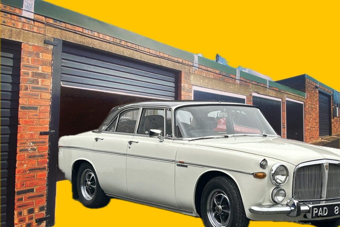 A classic rover motor car in front of a row of lock up garages